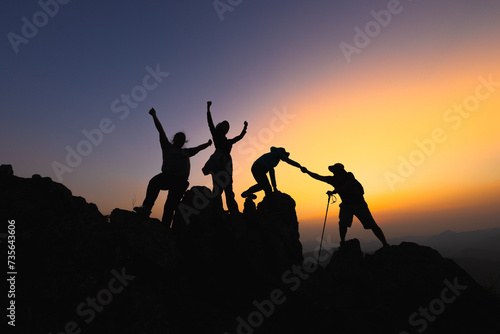  Silhouette Teamwork of four hiker helping each other on top of mountain climbing team beautiful sunrise. Teamwork friendship hiking help each other trust assistance. climbing team success.