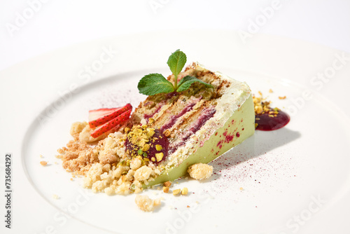Pistachio cake with a raspberry layer and crumbled cookie and pistachio topping on an isolated white background