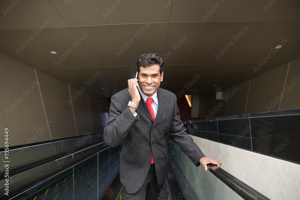 Indian businessman using his Smart phone on an escalator. Indian businessman using his Smart phone on an escalator.