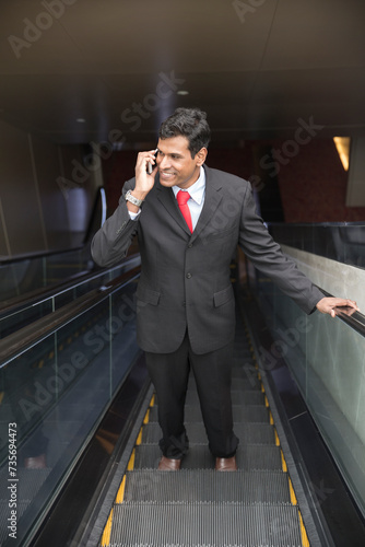 Indian businessman using his Smart phone on an escalator.