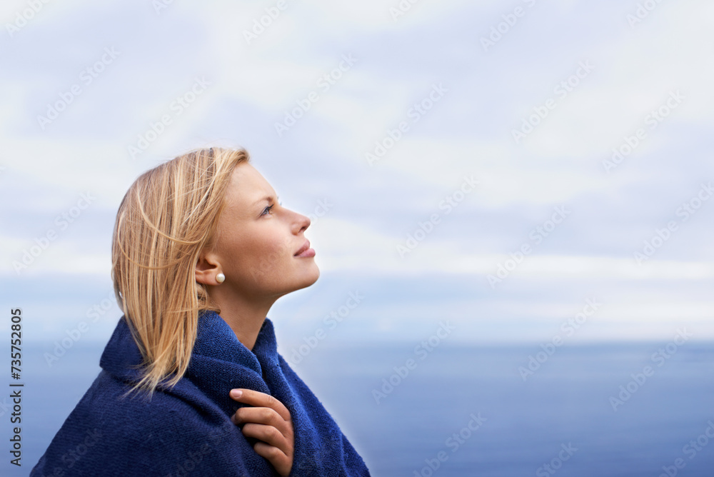 Thinking, ocean and woman with blanket with blue sky for adventure on holiday, vacation and weekend outdoors. Nature, travel and person by seaside for relaxing, happiness and peace in countryside