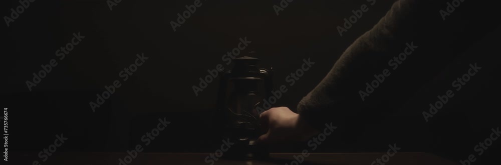 Anamorphic video of kerosene lamp light or an ancient lantern flickers in the dark. Old classic oil lantern burning with an orange flame. Male hand turn the lamp off.