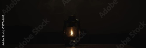 Anamorphic video of kerosene lamp light or an ancient lantern flickers in the dark. Old classic oil lantern burning with an orange flame. Male hand turn the lamp off.