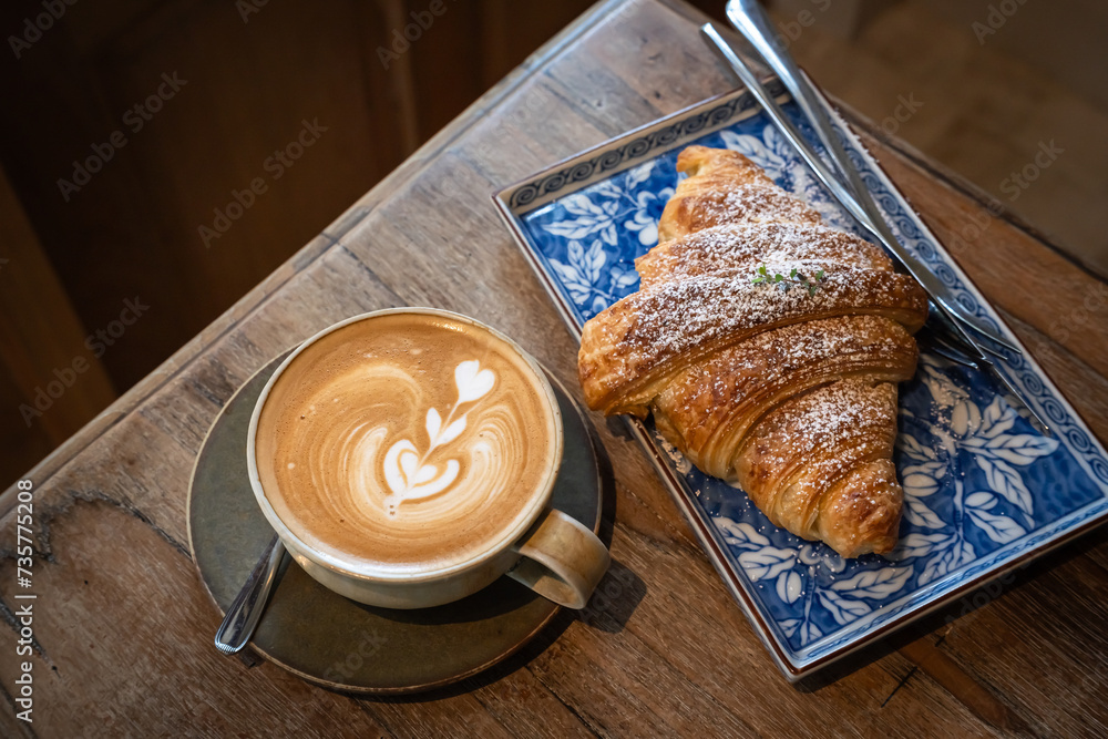 Hot coffee latte with latte art milk foam in cup mug with Croissant on wood desk on top view. As breakfast In a coffee shop at the cafe,during business work concept,vintage style