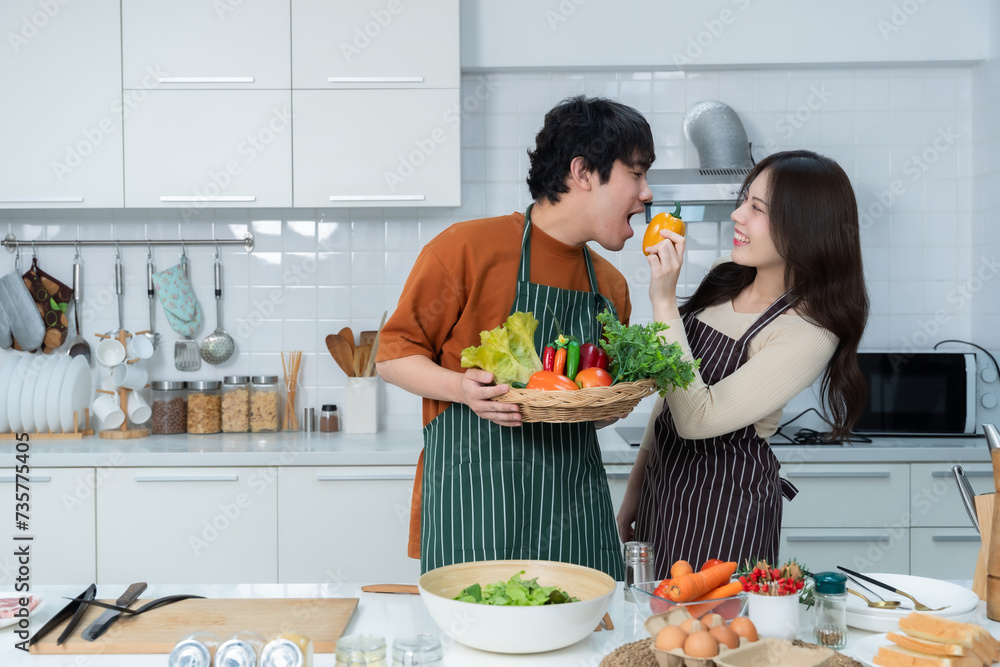 The young asian man who was tasting the food his girlfriend made preparing beef steak food and enjoy cook cooking with vegetables, meat, bread while standing on a kitchen Condo life or home