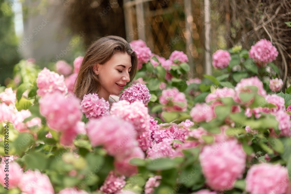 Hydrangeas Happy woman in pink dress amid hydrangeas. Large pink hydrangea caps surround woman. Sunny outdoor setting. Showcasing happy woman amid hydrangea bloom. Hydrangeas Happy woman in pink dress amid hydrangeas. Large pink hydrangea caps surround woman. Sunny outdoor setting. Showcasing happy woman amid hydrangea bloom.