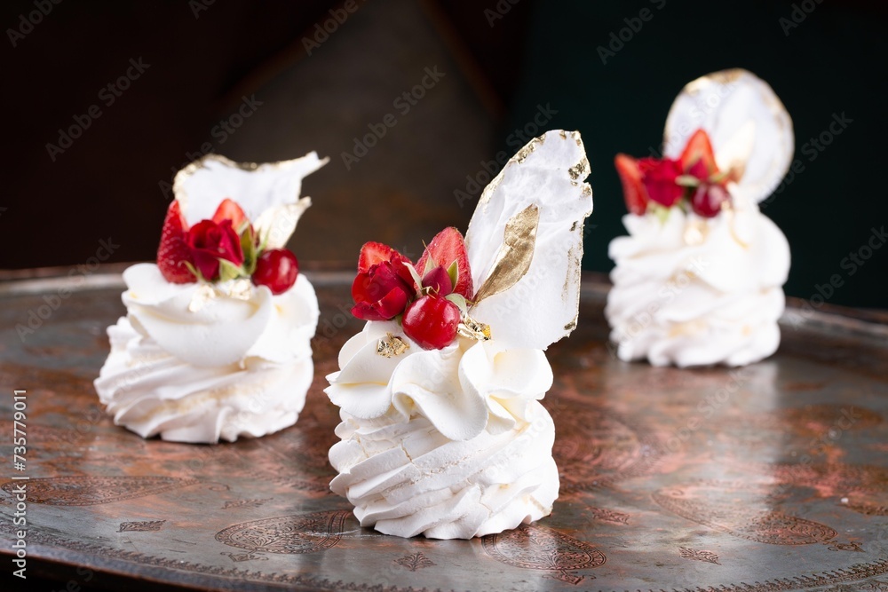 Small size single serve Pavlova dessert cakes decorated with red berries and strawberries on serving plate in restaurant, dark background