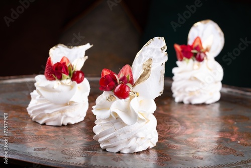 Small size single serve Pavlova dessert cakes decorated with red berries and strawberries on serving plate in restaurant  dark background