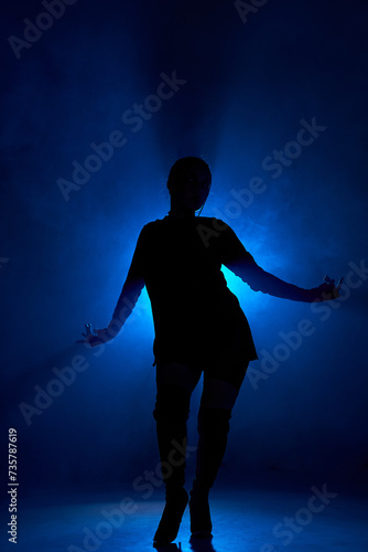 Silhoette of sexy woman dancing in dark smoky room with blue backlit. Unrecognizable lady with passionate body moving sensually alone in room, rehearsal, performance. portrait copy space