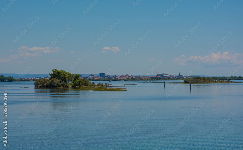 An island in the Grado section of the Marano and Grado Lagoon in Friuli-Venezia Giulia, north east Italy. Channel markers shows the edge of a navigable channel in the shallow waters. Grado town can be