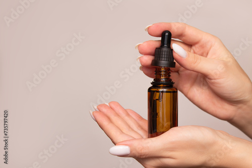A woman holds in her hands and opens a dark glass bottle with oil or serum. Isolated on a light background. Dropper with a cosmetic product for skin, face, hair or body. Self care and beauty concept