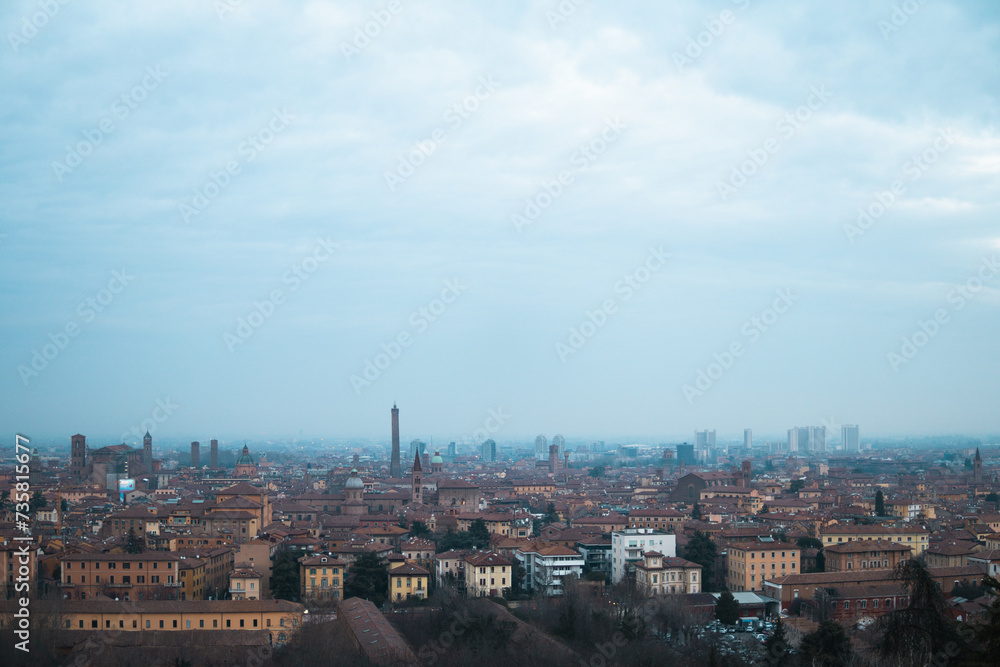 Captivating winter evening view from San Michele in Bosco, Bologna, showcasing the city skyline engulfed in mist against a moody gray cloudy sky.