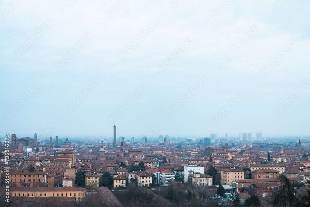 Captivating winter evening view from San Michele in Bosco, Bologna, showcasing the city skyline engulfed in mist against a moody gray cloudy sky.