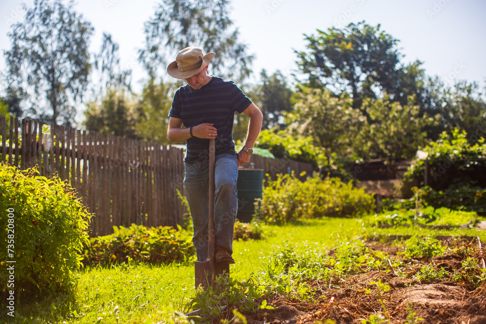 Fototapeta premium The farmer stands with a shovel in the garden. Preparing the soil for planting vegetables. Gardening concept. Agricultural work on the plantation