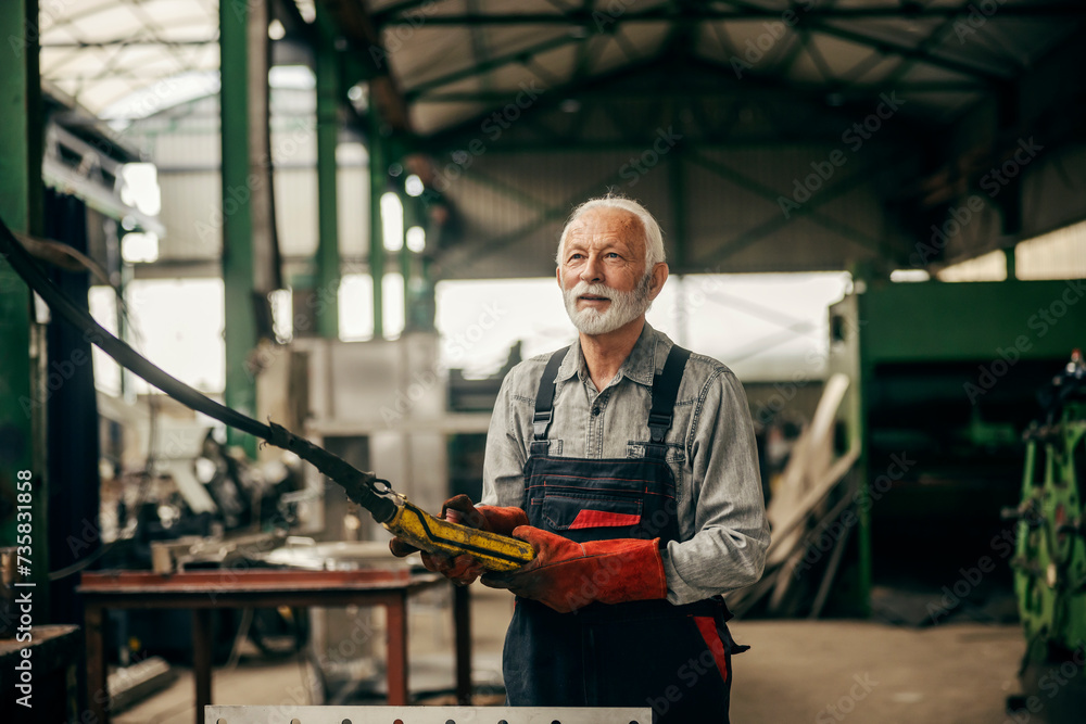 An older heavy industry worker is working at factory while manipulating machine. An older heavy industry worker is working at factory while manipulating machine.