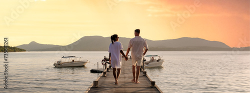 Fotografie couple walking on a wooden pier in the ocean at sunset in Thailand
