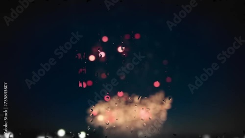 Fireworks flashes, blurred, in the background, a view through raindrops running down the glass. Holiday concept. 