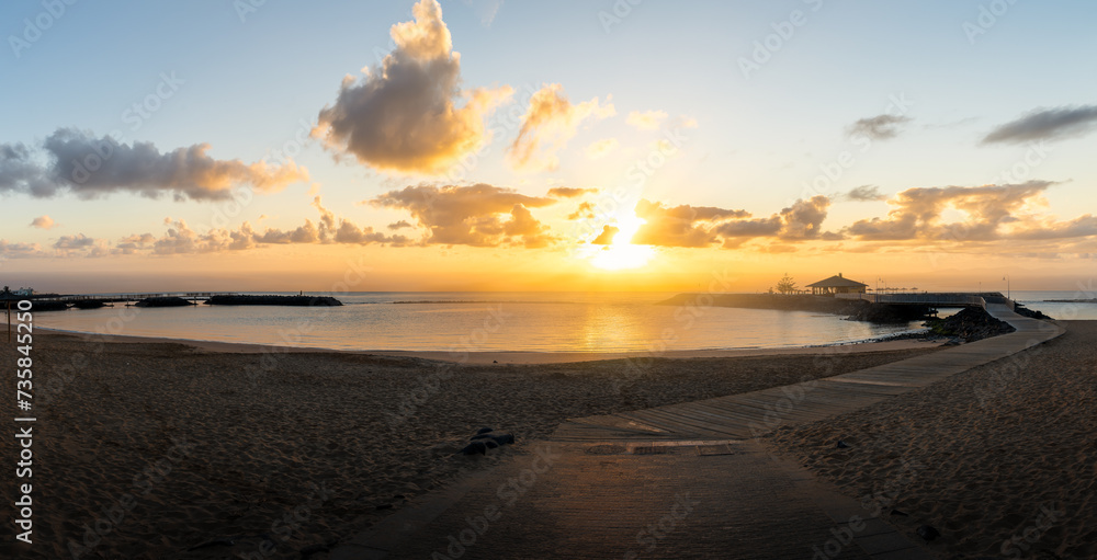Dawn breaks over La Guirra Beach, Caleta de Fuste, casting a peaceful golden glow across the tranquil waters of Fuerteventura