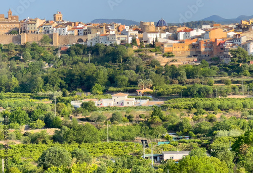 Rural landscape in Segorbe town. Farmhouse at vegetable field. Spain farmland. Cultivation of crops, production of food. House in farm field against backdrop of residential buildings in city photo