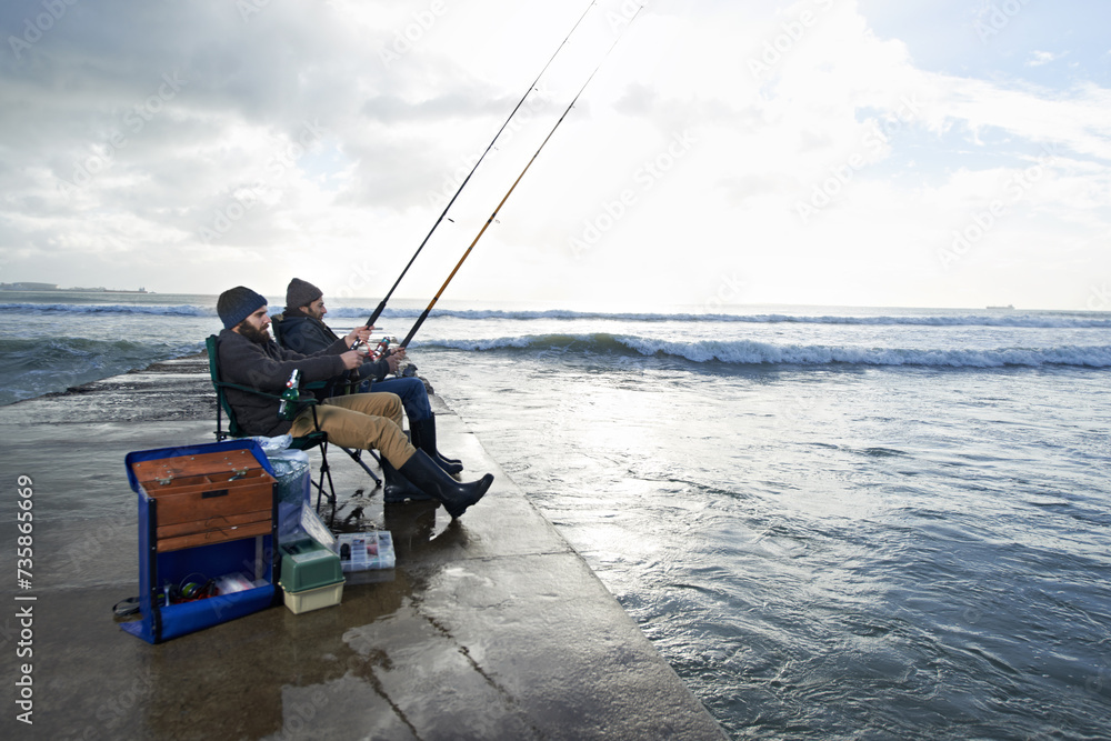 Friends, fisherman and men by ocean fishing with rod, reel and equipment to catch fish for hobby. Nature, sports and people cast a line for fun, relaxing or adventure on holiday, vacation and weekend Friends, fisherman and men by ocean fishing with rod, reel and equipment to catch fish for hobby. Nature, sports and people cast a line for fun, relaxing or adventure on holiday, vacation and weekend