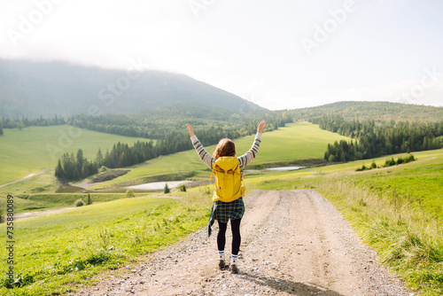 Young Woman walking on through green grass valley on background big mountains. Tourist traveler on background valley. Hiker resting.