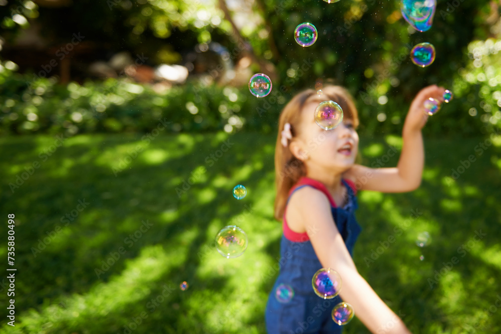 Child, bubbles and garden grass for playing in summer sunshine in backyard for holiday, carefree or happy. Kid, girl and youth in California in outdoor nature or fun for vacation, weekend or game