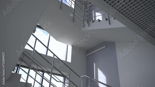 Empty staircase with shiny metal railings in hall with white walls and large windows. Minimalist interior design of multistory building photo