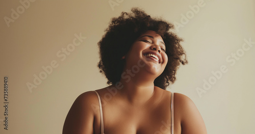 Studio portrait of youthful curvy black girl in camisole laughing, brown short hair, beige background photo