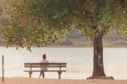 femme assise seule sur un banc au bord d'un lac en automne