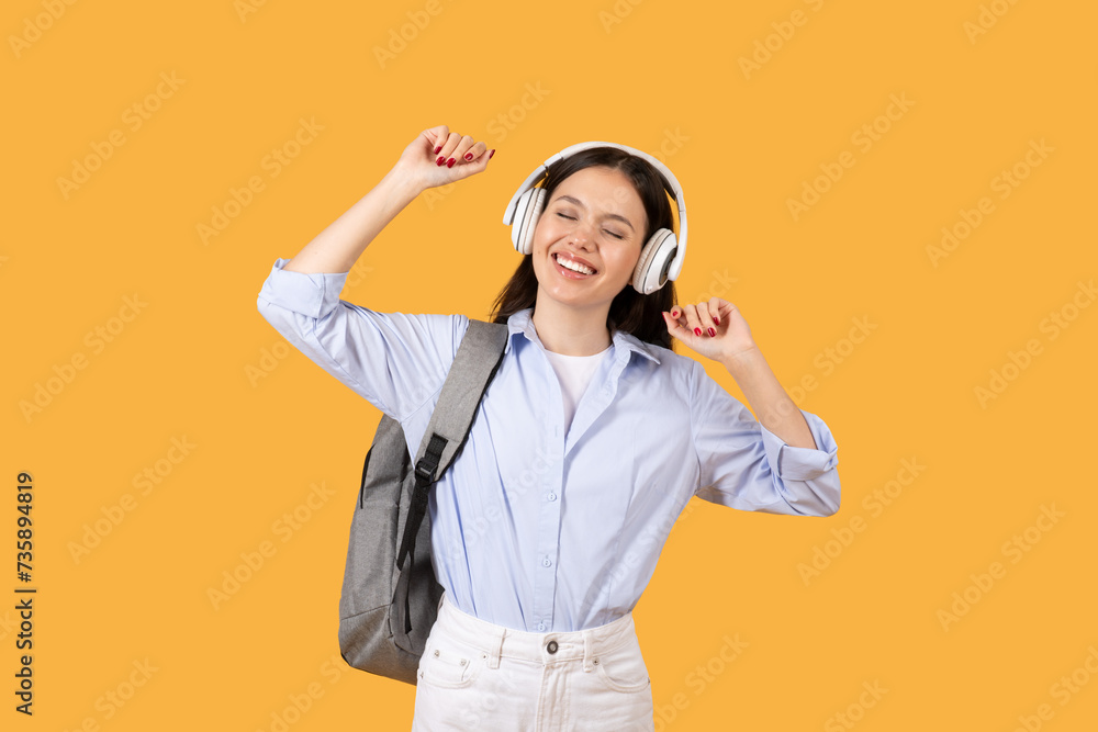 Joyful female student dancing with headphones on, yellow backdrop Joyful female student dancing with headphones on, yellow backdrop