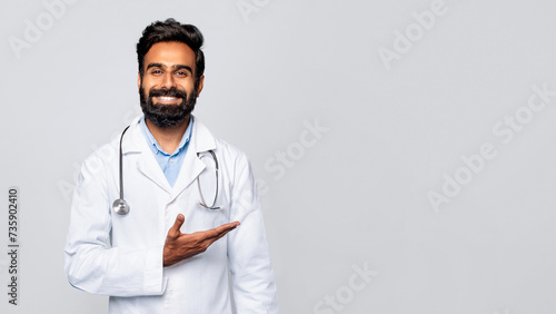 Inviting indian male doctor gesturing with hand aside on grey background photo