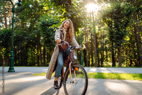 Young woman in stylish clothes rides a bicycle in a sunny park. Active lifestyle. © maxbelchenko