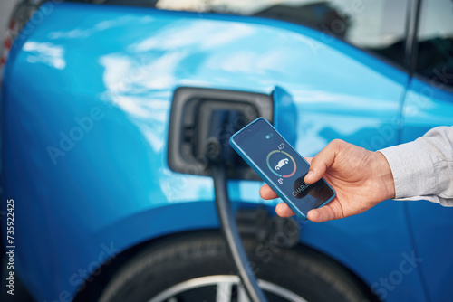 Charging process on the display of smartphone. Man with blue electric car on the station