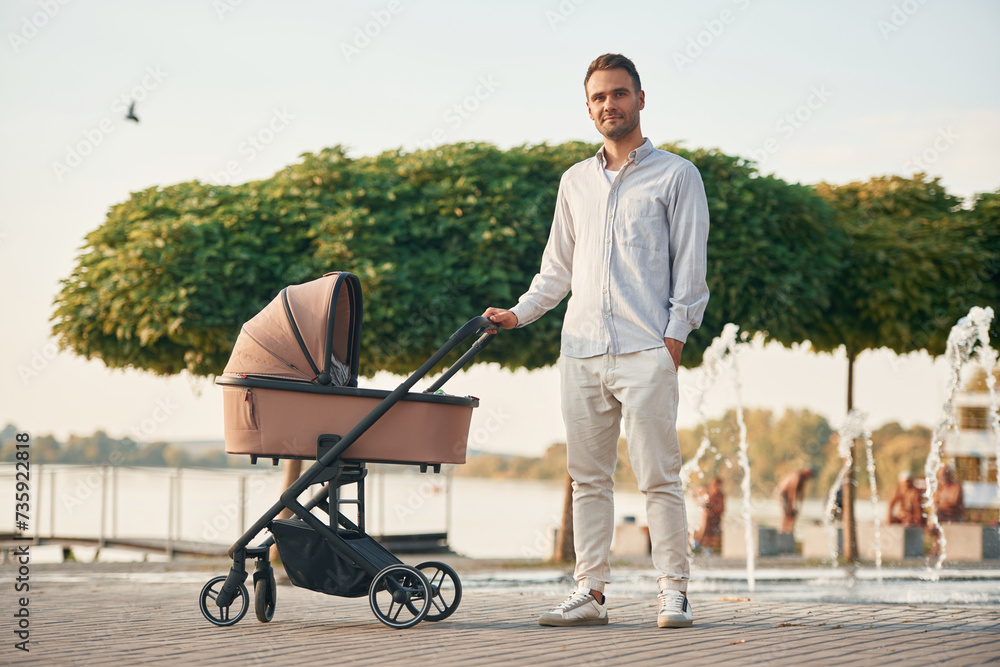 Young father is outdoors, standing with pram