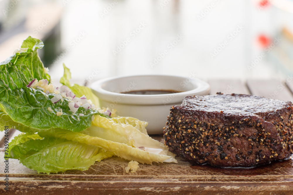 Close up of Pepper steak with lettuce, raw onions and gravy on wooden board in restaurant Close up of Pepper steak with lettuce, raw onions and gravy on wooden board in restaurant