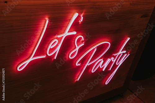 Señal de luz roja que dice let'&party. Letrero luminoso en pared de madera. photo