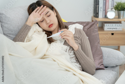 Young Asian woman having high fever while checking body temperature, female sneezing and runny nose with seasonal influenza, allergic, digital thermometer, virus, coronavirus, illness, respiratory