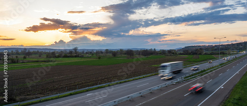 Transportation trucks in high speed driving on a highway through rural landscape. Fast blurred motion drive on the freeway. Freight scene on the motorway.