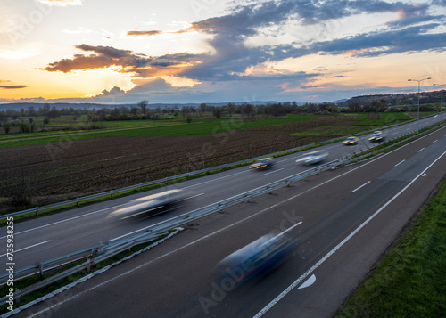 Cars drive at high speed on the highway through the rural landscape. Fast blurred highway driving. A scene of speeding on the highway.
