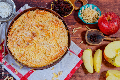 Freshly baked apple pie on a rustic kitchen worktop with ingredients and kitchen utensils.