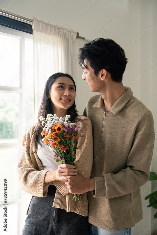 Romantic young asian couple embracing with holding flowers and smiling in living room at home. fall in love. Valentine concept Romantic young asian couple embracing with holding flowers and smiling in living room at home. fall in love. Valentine concept