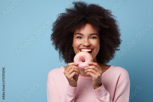 Close up young happy woman in casual sweater hold sweet pink cream donuts biting chocolate bar look camera isolated on plain pastel light blue background studio portrait. People lifestyle food concep