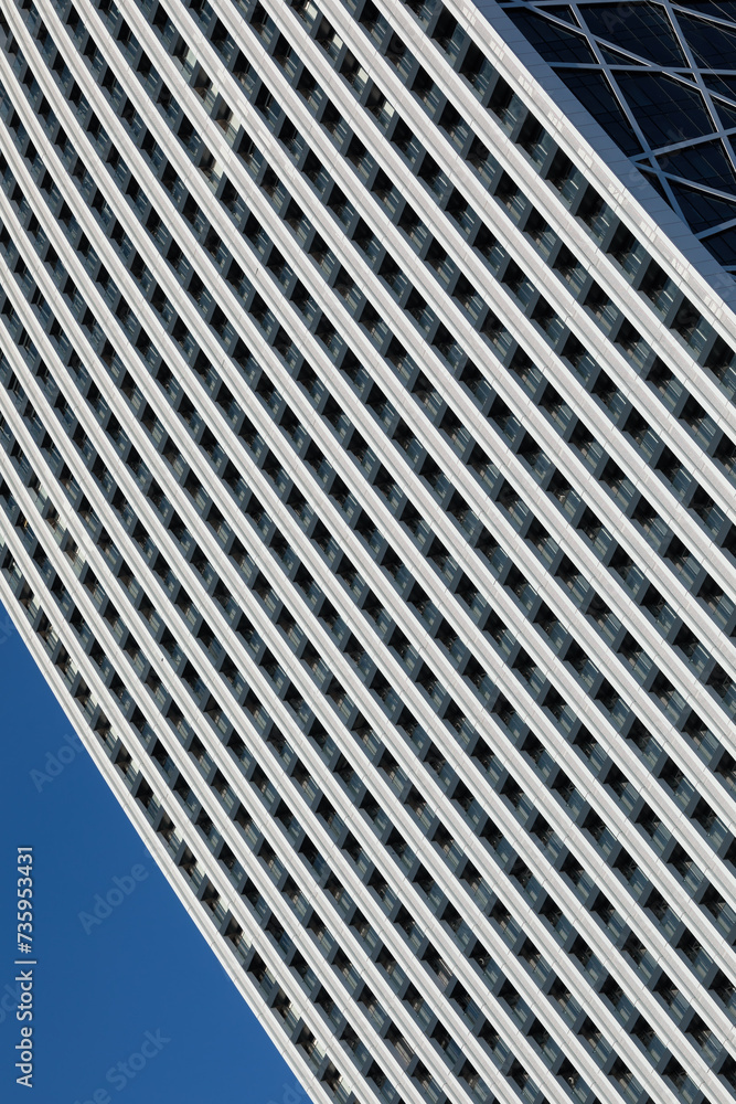 A minimalistic photo of a part of a modern building with repetitive pattern on its exterior stands out against the clear blue sky