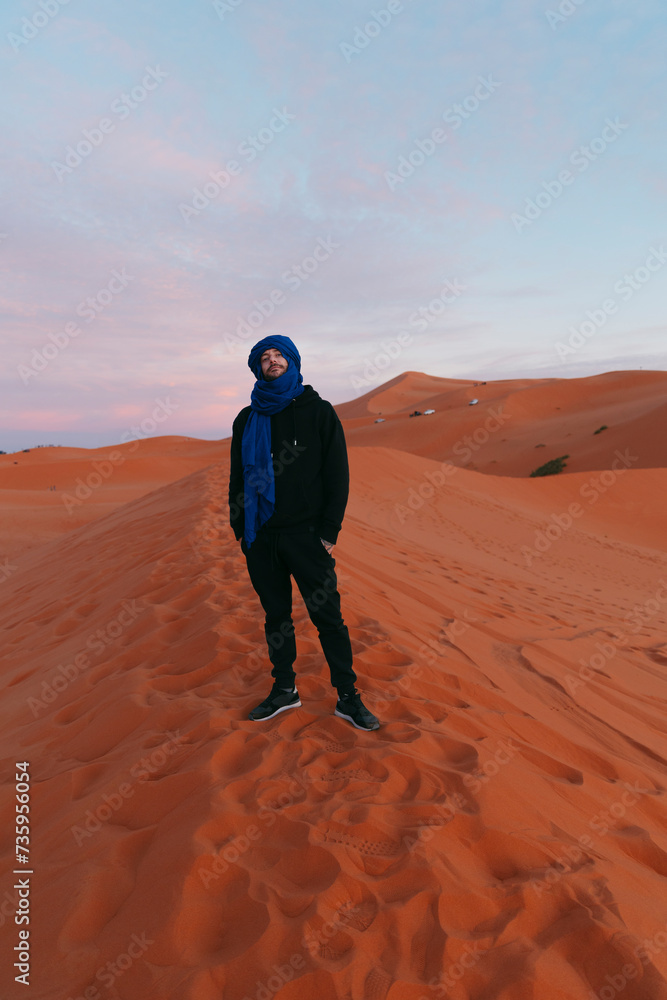 General view of a man with a Berber scarf from the top of a dune in the Sahara desert