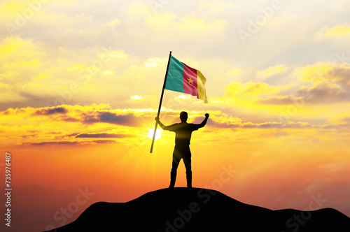 Cameroon flag being waved by a man celebrating success at the top of a mountain against sunset or sunrise. Cameroon flag for Independence Day.