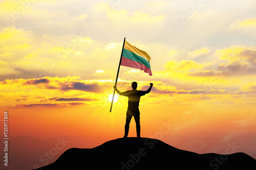 Lithuania flag being waved by a man celebrating success at the top of a mountain against sunset or sunrise. Lithuania flag for Independence Day. ©  minionionniloy
