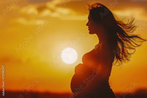 Silhouette of pregnant mother outdoors. Windblown hair. Sunset lighting.