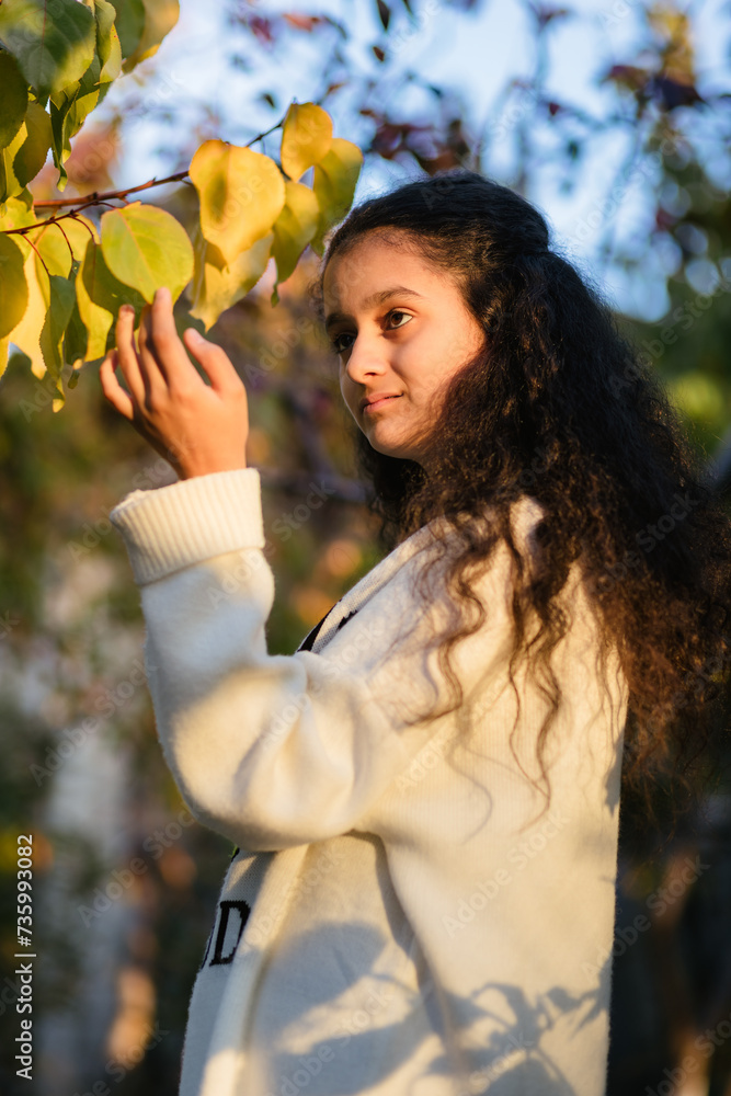 Autumn portrait of cute 13 years old girl touching apricot leaves in sunset