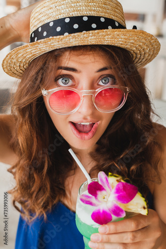 attractive young woman in blue dress and straw hat wearing pink sunglasses drinking cocktails