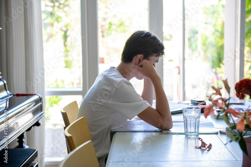 Teenage boy sitting at the dining room table, upset and depressed photo
